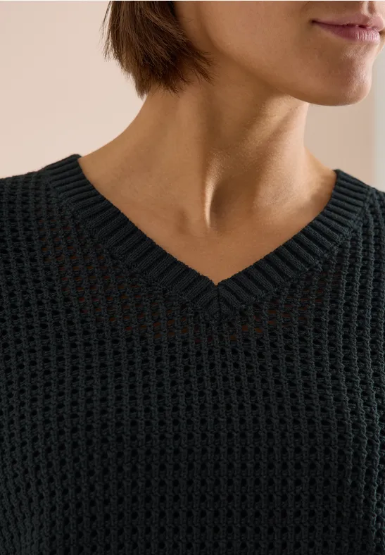 Close-up van een torso in een zwarte grofgebreide trui met V-hals.