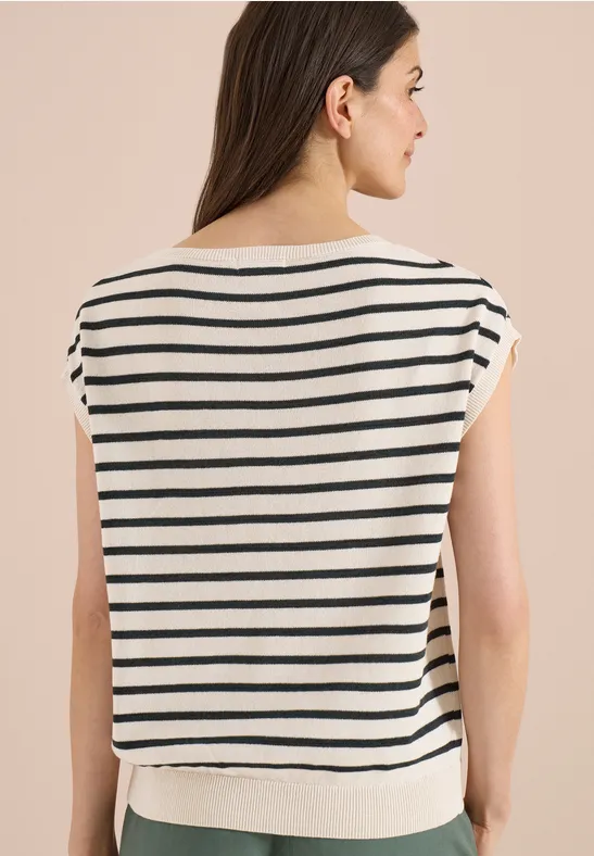 Frau von hinten in weiß-blau gestreiftem kurzärmligem Shirt vor beigem Hintergrund.