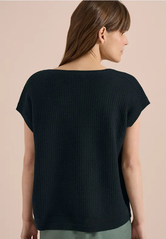 Vrouw van achteren in een zwart ribgebreid shirt met korte mouwen voor een beige achtergrond.