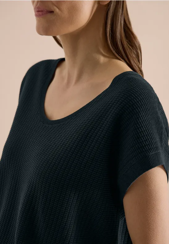 Close-up van een vrouw in een zwart, gestructureerd T-shirt met korte mouwen.