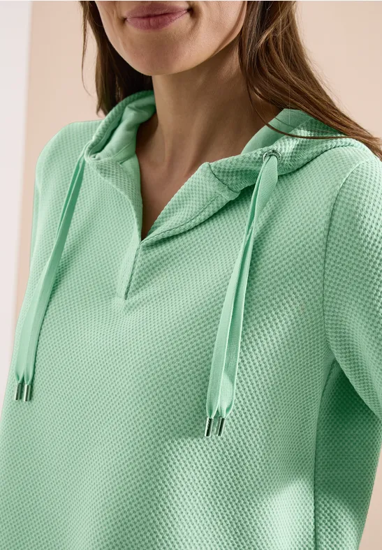 Frau in mintgrünem, strukturiertem Hoodie mit V-Ausschnitt und Kordelzügen.