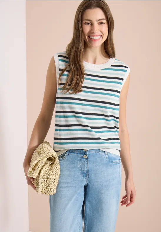 Frau in gestreiftem ärmellosen Top, hellen Jeans und Strohtasche in der Hand.