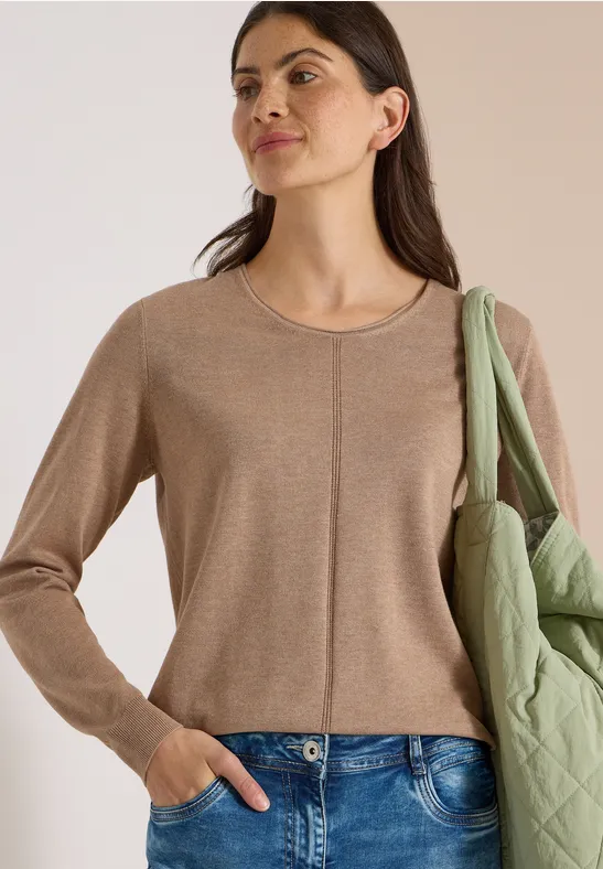 Femme portant un pull beige à col rond, un jean et un sac matelassé vert sur l’épaule.