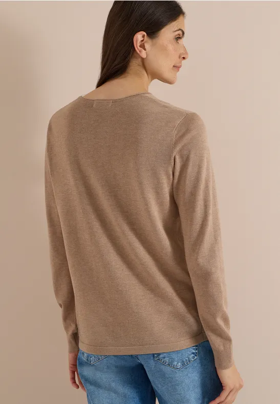 Femme vue de dos portant un pull beige et un jean, fond neutre.