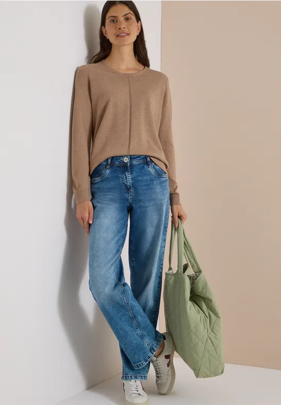 Femme en pull beige, jean ample et baskets blanches, portant un sac matelassé vert.