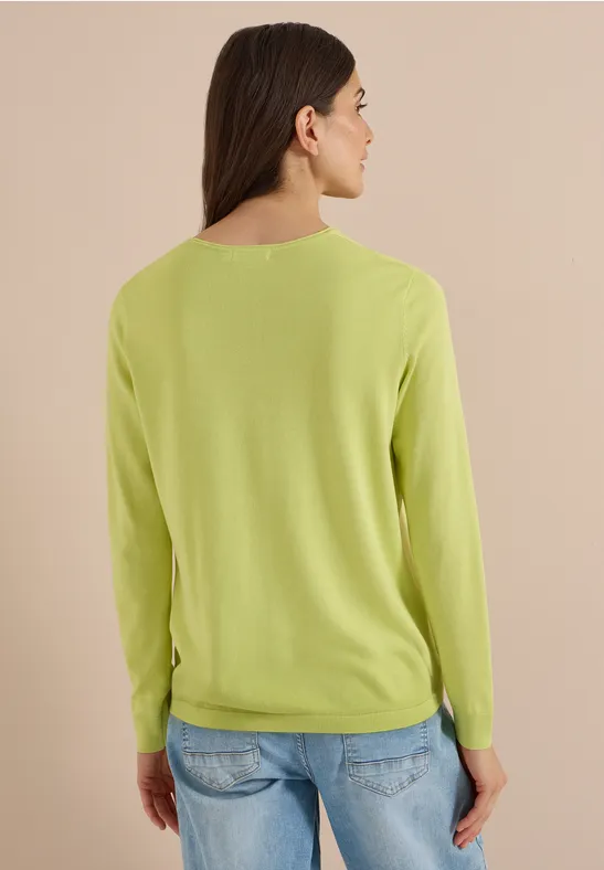 Vue de dos d’une personne portant un pull vert clair et un jean bleu sur fond beige.