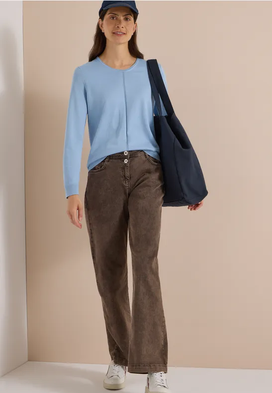 Femme portant un cardigan bleu clair, pantalon en velours côtelé marron, baskets blanches, casquette et sac bleu marine.