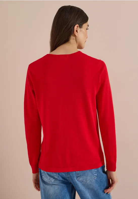 Femme vue de dos portant un haut rouge à manches longues et un jean bleu sur fond beige.