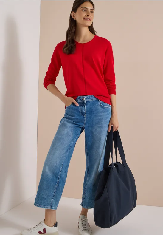 Femme en pull rouge, jean ample et baskets blanches, portant un grand sac bleu marine.