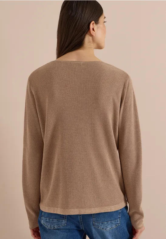 Frau von hinten in beige Pullover und blauen Jeans, steht vor hellem Hintergrund.