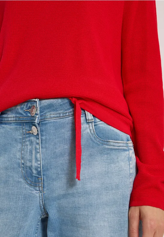 Rotes Langarmshirt mit Knoten vorn, kombiniert mit hellblauen Jeanshose.