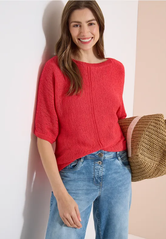 Femme en pull rouge à manches courtes, jean et chapeau de paille.