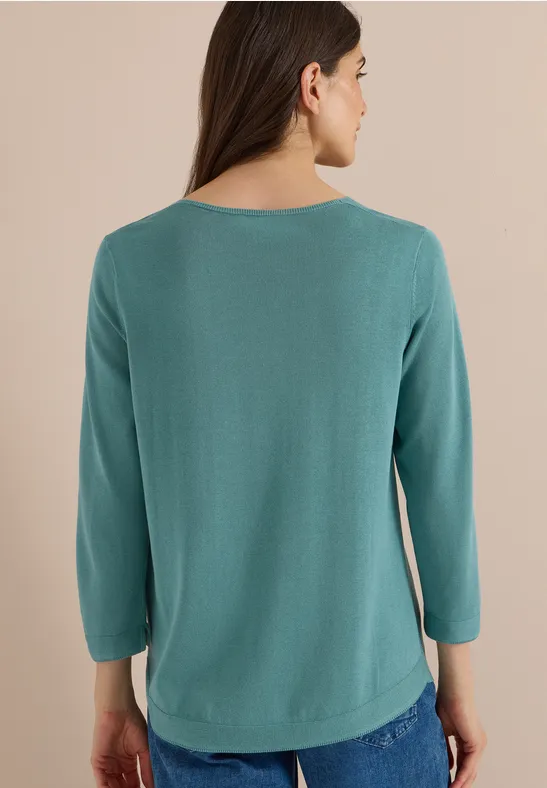 Frau von hinten trägt smaragdgrünes Langarmshirt und blaue Jeans.