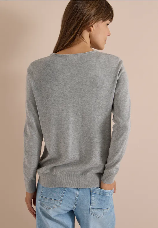 Femme vue de dos, en pull gris et jean bleu devant un fond beige.