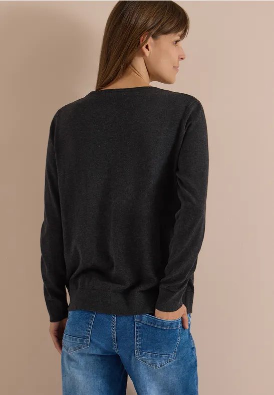 Femme de dos portant un pull noir et un jean bleu sur fond neutre.