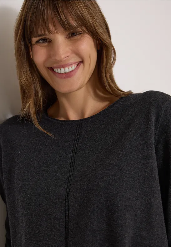Femme souriante aux cheveux châtains à frange, vêtue d'un pull gris, regard chaleureux vers l'appareil photo.