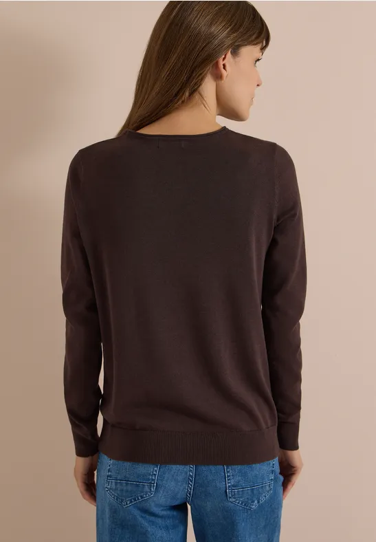 Personne de dos portant un pull marron et un jean bleu devant un fond neutre.