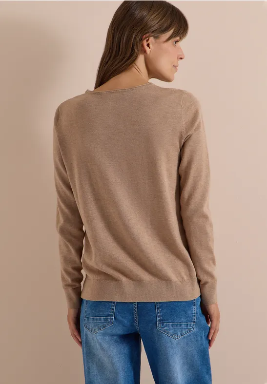 Rückansicht einer Frau in beigem Pullover und blauer Jeans vor hellem Hintergrund.