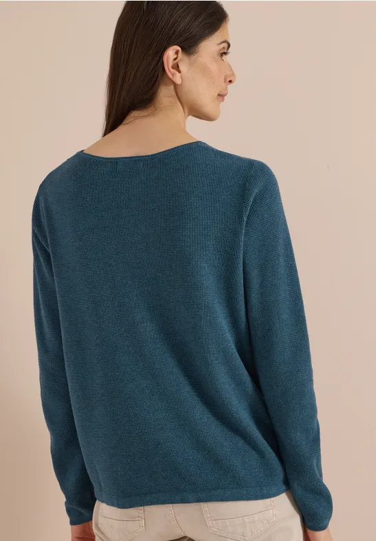 Eine Frau ist von hinten zu sehen und trägt einen schlichten, blauen Pullover.