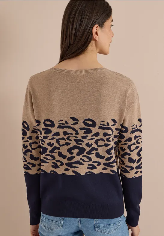 Eine Frau trägt einen Pullover in Camel und Marine mit blauem Leopardenmuster.