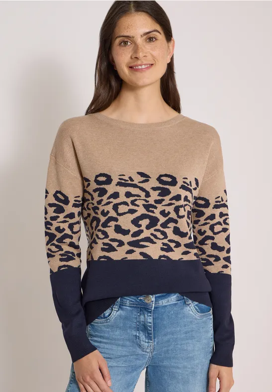 Frau trägt beigen Pullover mit Leopardenmuster und blaue Jeans