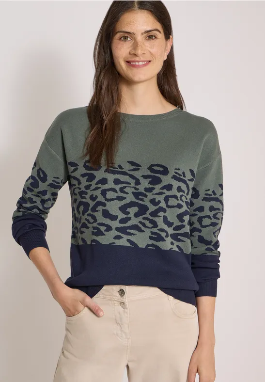 Frau trägt grünen Pullover mit dunkelblauem Leopardenmuster und heller Hose