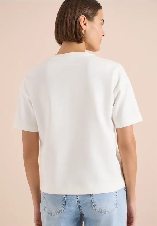 Osoba widziana od tyłu w prostym białym t-shircie i niebieskich jeansach.