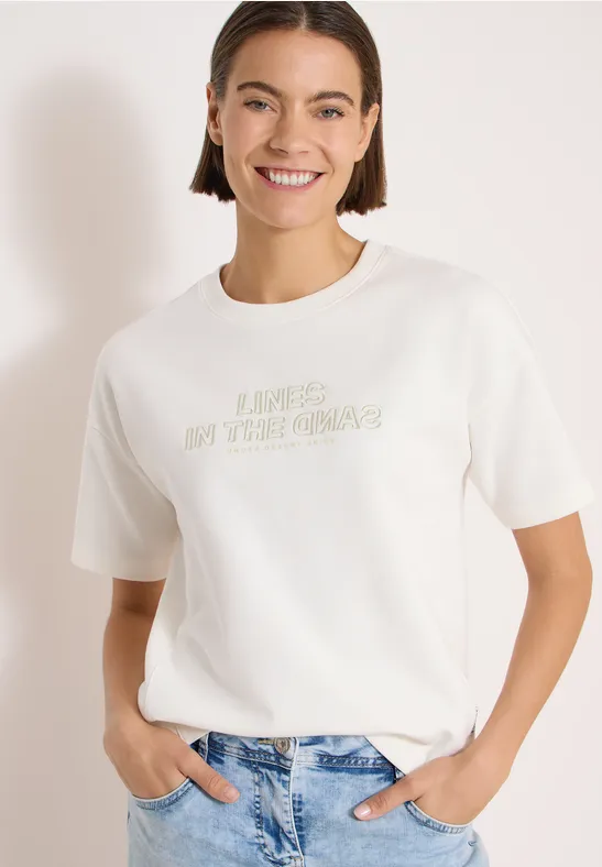 Kobieta w białym t-shircie z napisem i niebieskich dżinsach na białym tle.