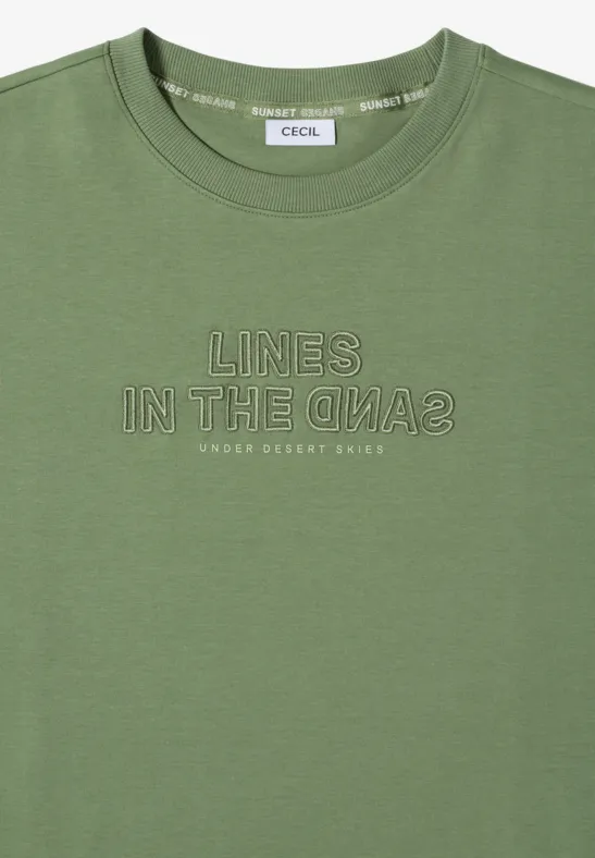 Oliwkowy t-shirt z krótkim rękawem, białym nadrukiem 'LINES IN THE SAND2' i małym napisem 'UNDER DESERT SKIES'.