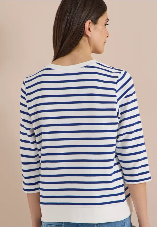 Femme vue de dos portant un t-shirt à manches longues blanc à rayures bleues
