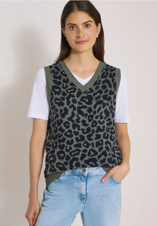 Frau trägt grüne Strickweste mit schwarzem Leopardenmuster, weißem T-Shirt und blauen Jeans.
