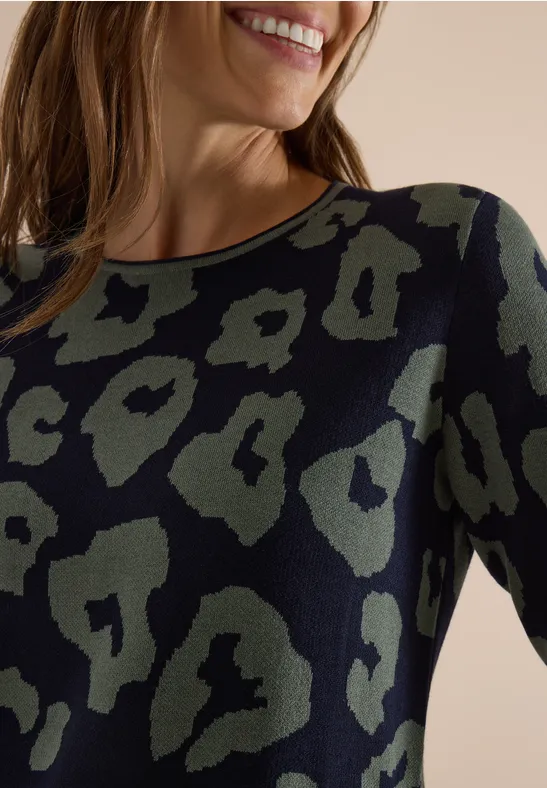 Vrouw lacht in close-up en draagt een shirt met kaki-zwart luipaardprint en lange mouwen.