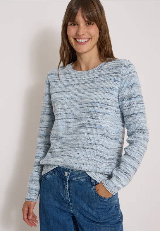 Femme souriante portant un pull tricoté bleu-gris et un jean, sur fond clair.