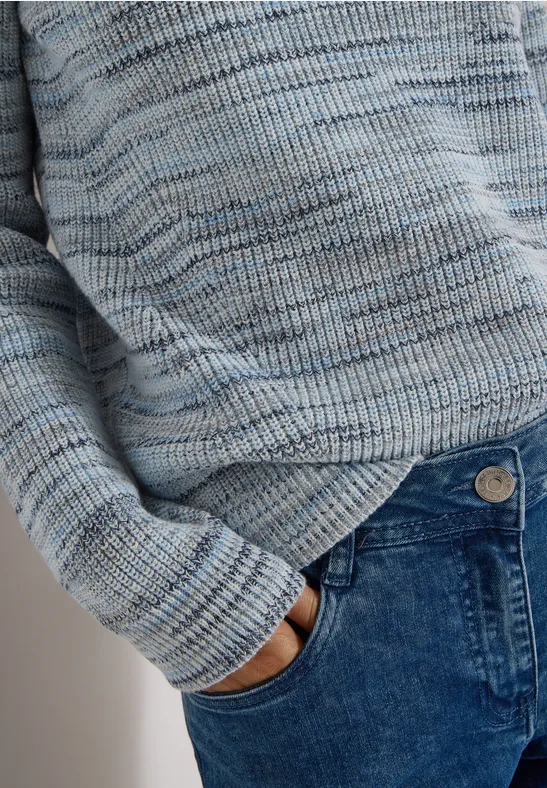 Personne porte un pull en tricot bleu clair et a la main dans la poche avant d'un jean bleu.
