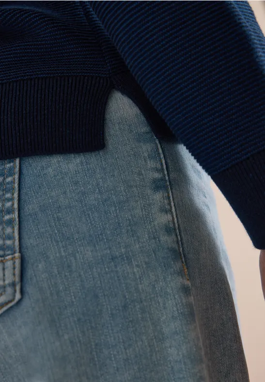 Gros plan d’un pull en maille bleu porté sur un jean clair.