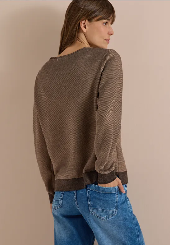 Femme de dos portant un pull marron et un jean bleu sur fond beige.