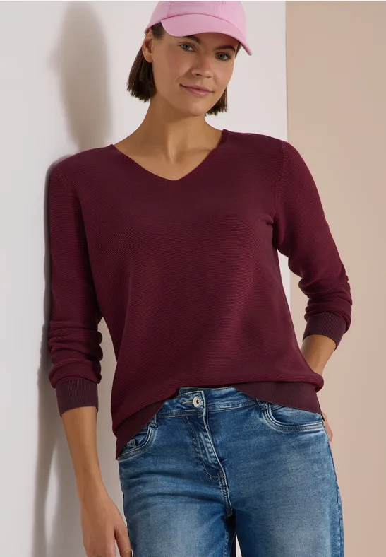 Femme en jean, pull bordeaux et casquette rose.