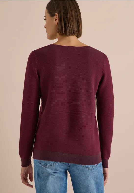 Femme vue de dos portant un pull fin bordeaux et un jean bleu clair.