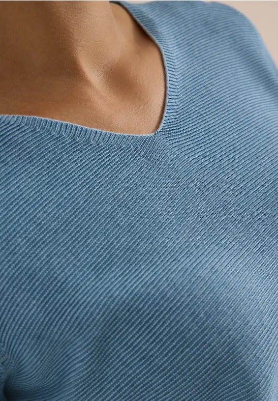 Gros plan sur un torse vêtu d'un pull col V côtelé bleu clair.