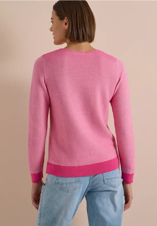 Femme de dos portant un pull rose et un jean bleu clair sur un fond neutre.