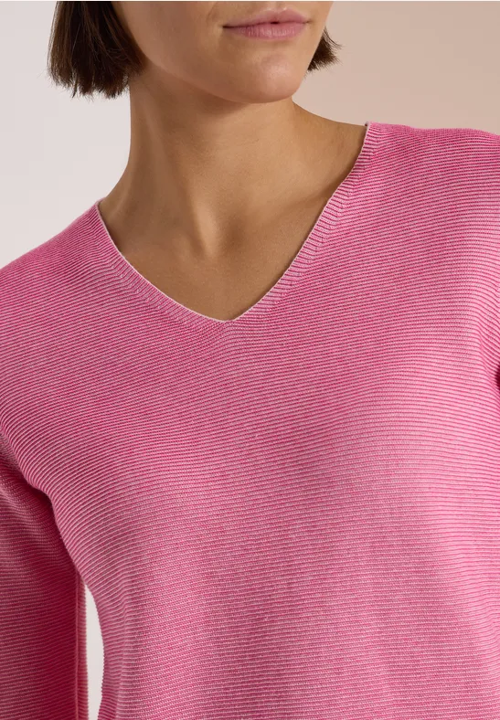 Femme portant un pull rose à col V, buste visible, fond discret.