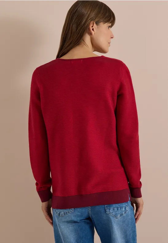 Femme de dos avec pull rouge et jean bleu.
