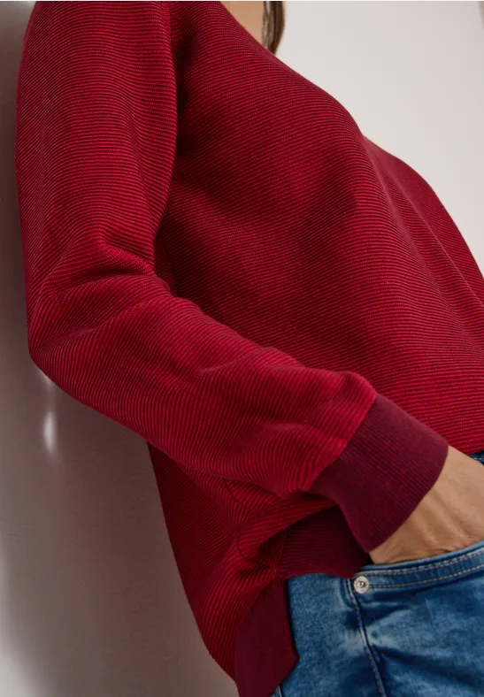 Vue latérale d'une personne en pull rouge et jeans bleus, la main dans la poche.