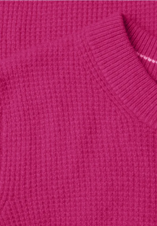 Nahaufnahme eines pinken Strickpullovers mit Waffelmuster und Rundhalsausschnitt