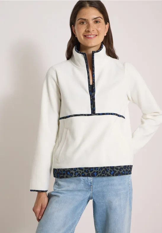 Vrouw in witte fleece trui met halve rits en dessindetails, glimlachend.