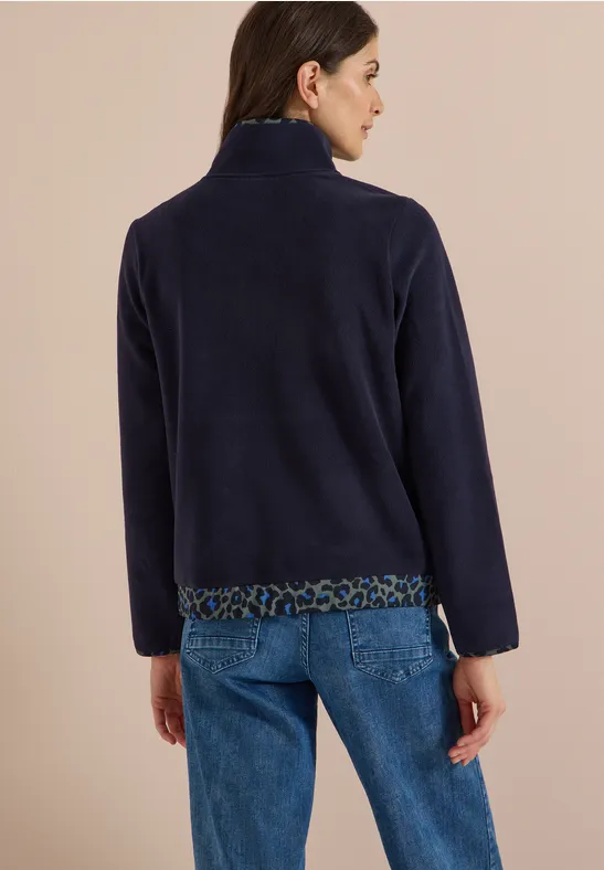 Vrouw van achteren in marineblauwe fleecetrui met luipaardprintbies en spijkerbroek, beige achtergrond