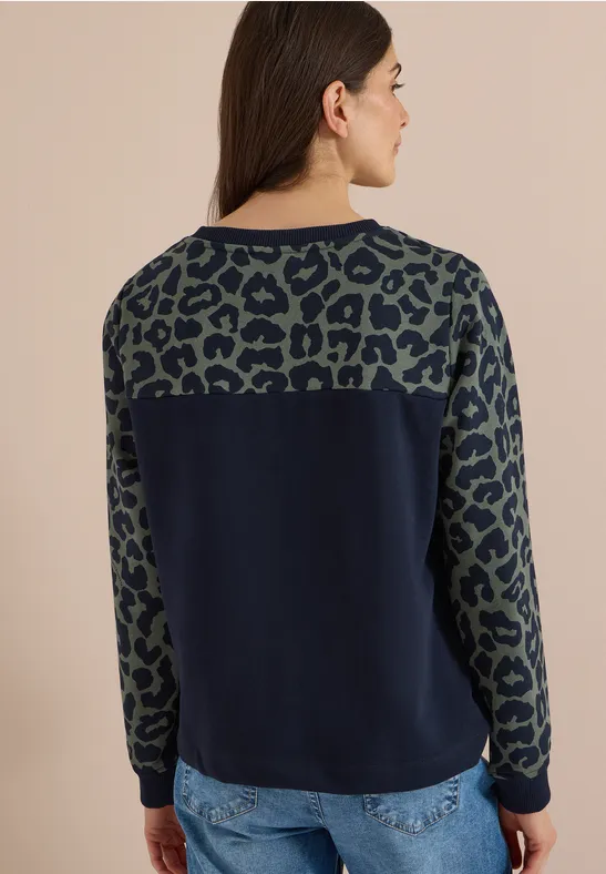 Frau im Profil, dunkelblauer Pullover mit olivgrünen Leopardenmustern an Ärmeln und oberem Rücken.