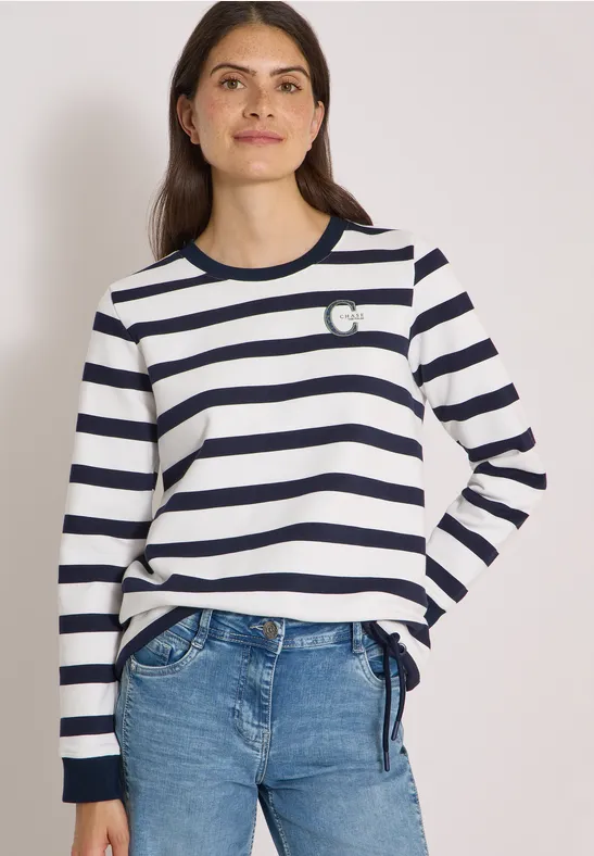 Femme en t-shirt manches longues blanc à rayures bleues, petit cœur brodé, portée avec un jean.