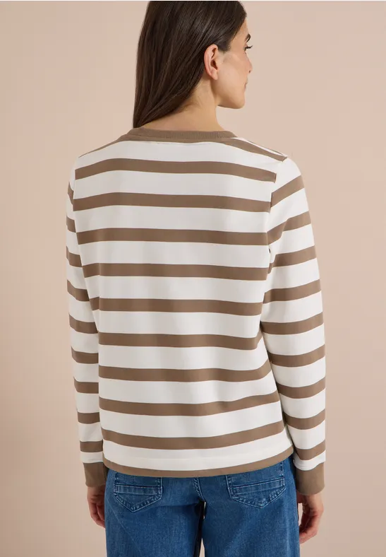 Frau von hinten in Jeans und gestreiftem Langarmshirt vor neutralem Hintergrund.