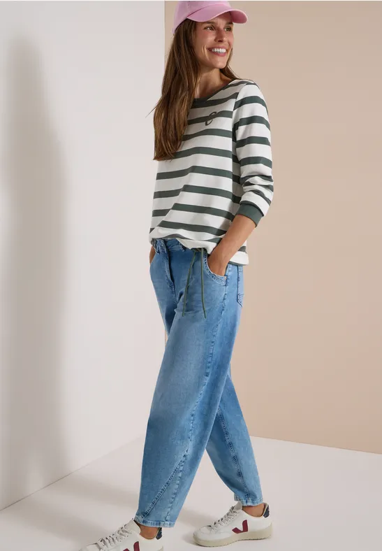Une femme souriante porte un t-shirt rayé, un jean et une casquette